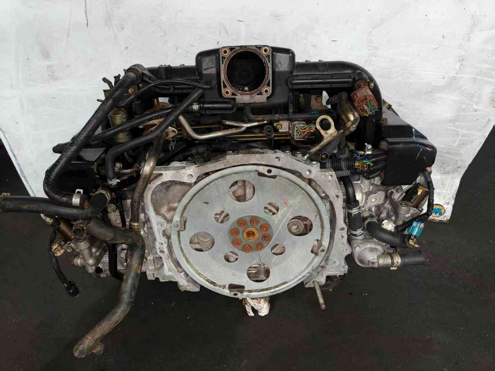 Subaru EZ30 engine assembly rear view showing flywheel mounting plate, wiring harness and coolant hoses