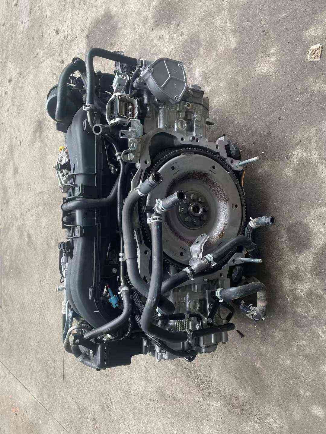 Subaru FA20 naturally aspirated engine assembly rear view showing flywheel, intake manifold and coolant hoses