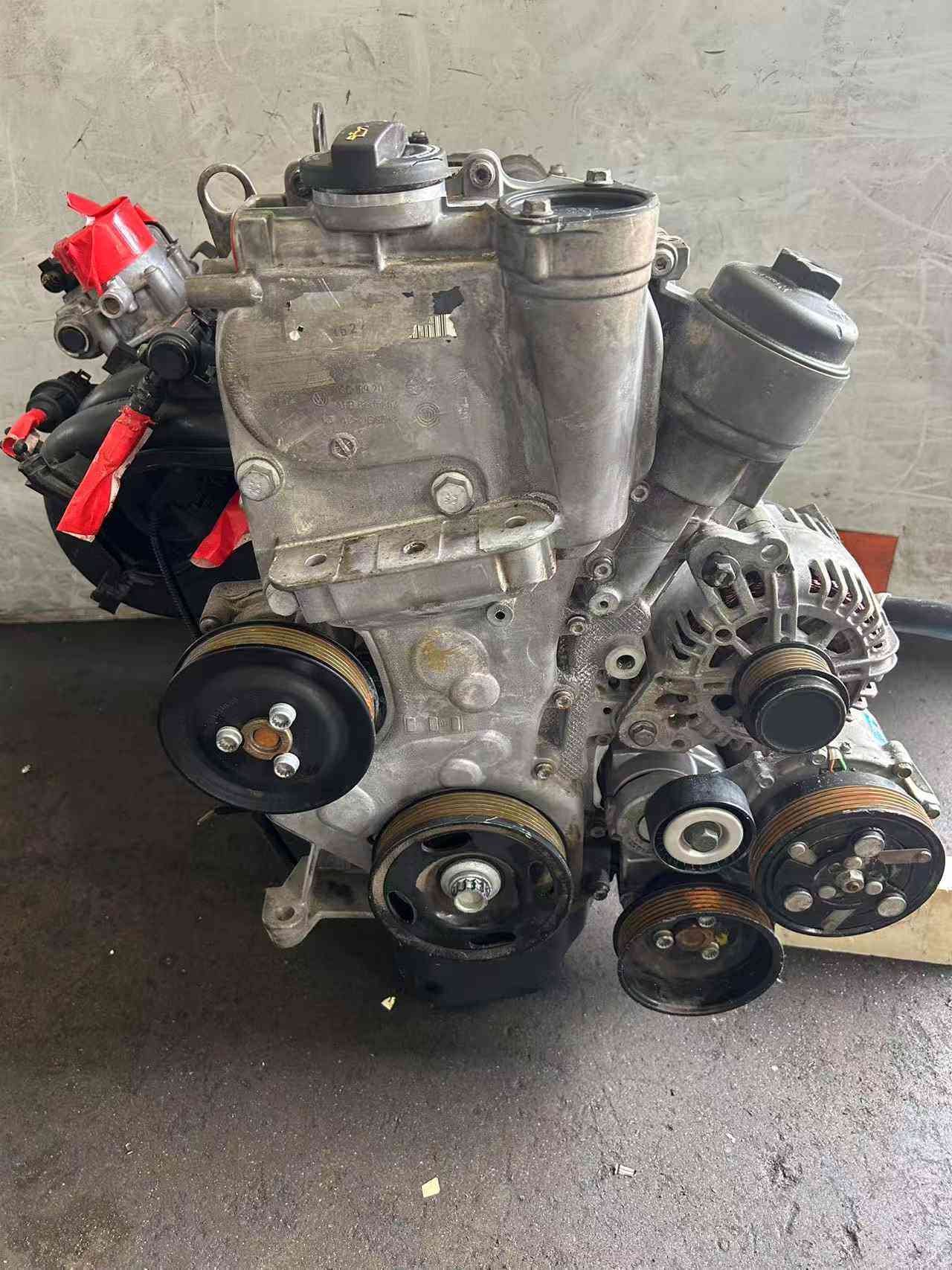 Volkswagen EA111 CLP engine front view with alternator, air-conditioning compressor, and multi-rib accessory pulleys.