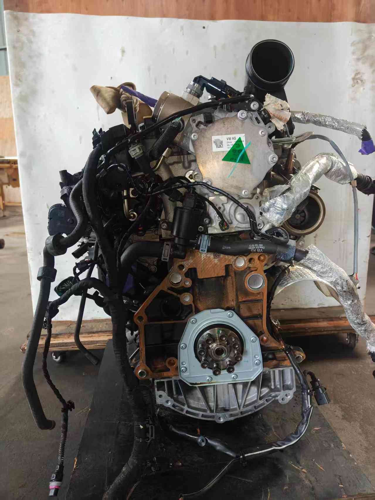 Flywheel-side view of a Volkswagen EA888 Gen 3 CHH engine with rear crankshaft flange, heat-shielded piping, and wiring harness.